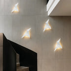 Geometric white bird-shaped wall lights emit a warm glow; metal and acrylic sculptural fixtures.
