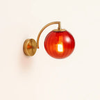 Warm glow from ribbed red glass globe and curved brass arm; timeless, elegant illumination.