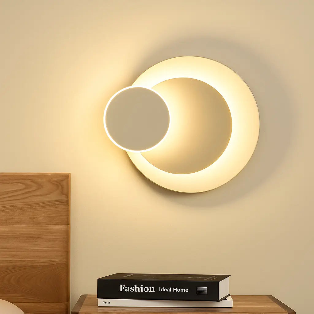 A modern adjustable round LED metal wall sconce glowing softly against a plain wall.