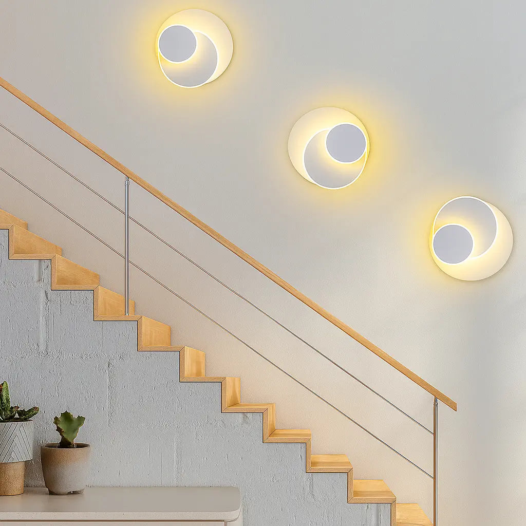 Three modern round LED metal wall sconces with overlapping circles glow warmly on a white wall.