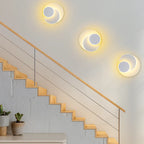 Three modern round LED metal wall sconces with overlapping circles glow warmly on a white wall.
