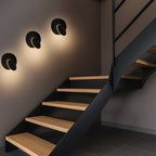 Three modern round LED wall sconces softly cast contemporary light across a gray wall.