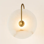 Minimalist circular LED wall lamp with white translucent shade and brass fixture, softly glowing.