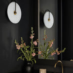 A circular, minimalist LED wall lamp with a sleek modern design mounted on a black wall.