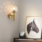 The Helena Modern Industrial Glass Wall Light with gold base and round glass shade.