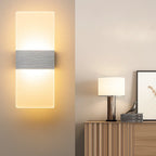 Rectangular brushed metal and acrylic LED wall sconce glowing softly on a beige wall.