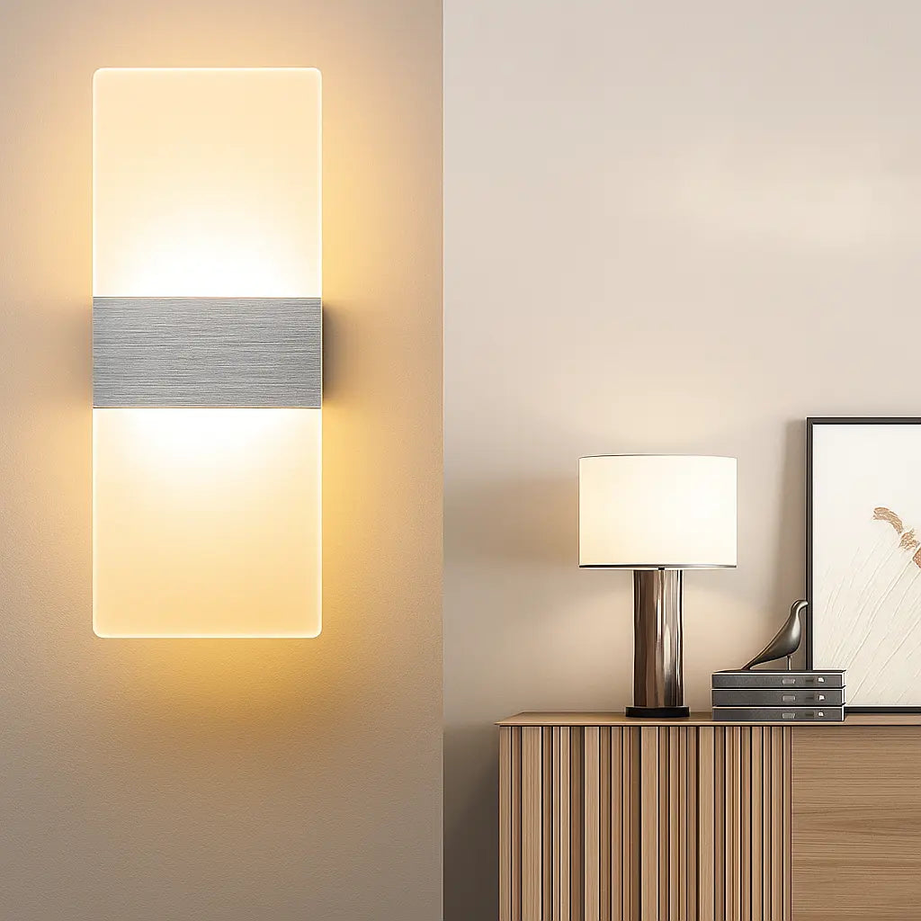Rectangular brushed metal and acrylic LED wall sconce glowing softly on a beige wall.