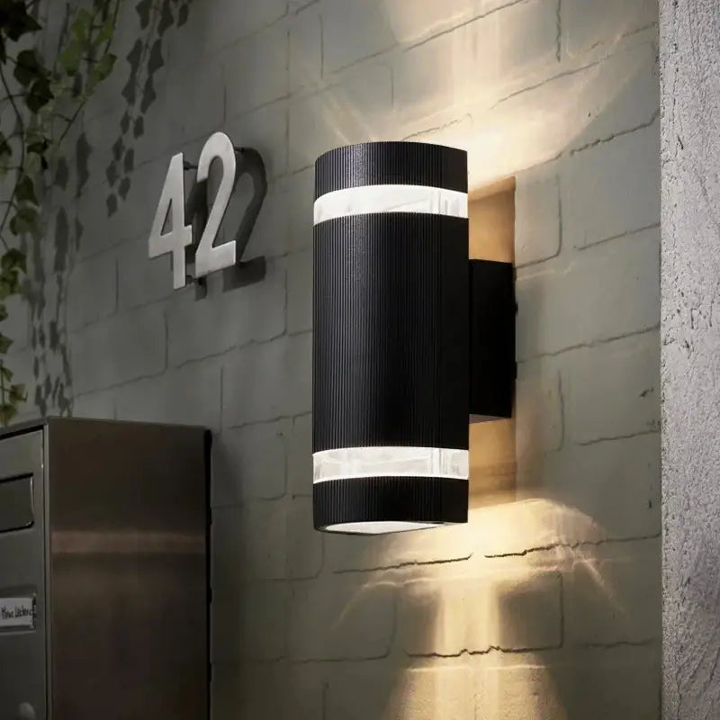 A Classic Cylinder LED-compatible Black Outdoor Wall Light with sleek design casts striking patterns.