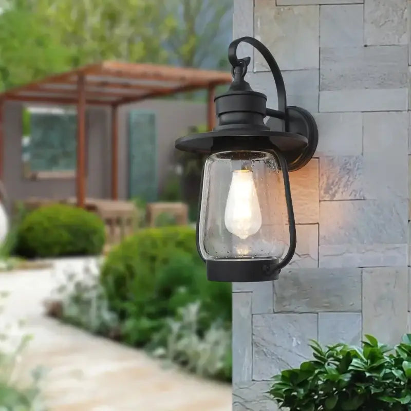 A black metal wall light with bubble glass is mounted on a stone wall, illuminated.