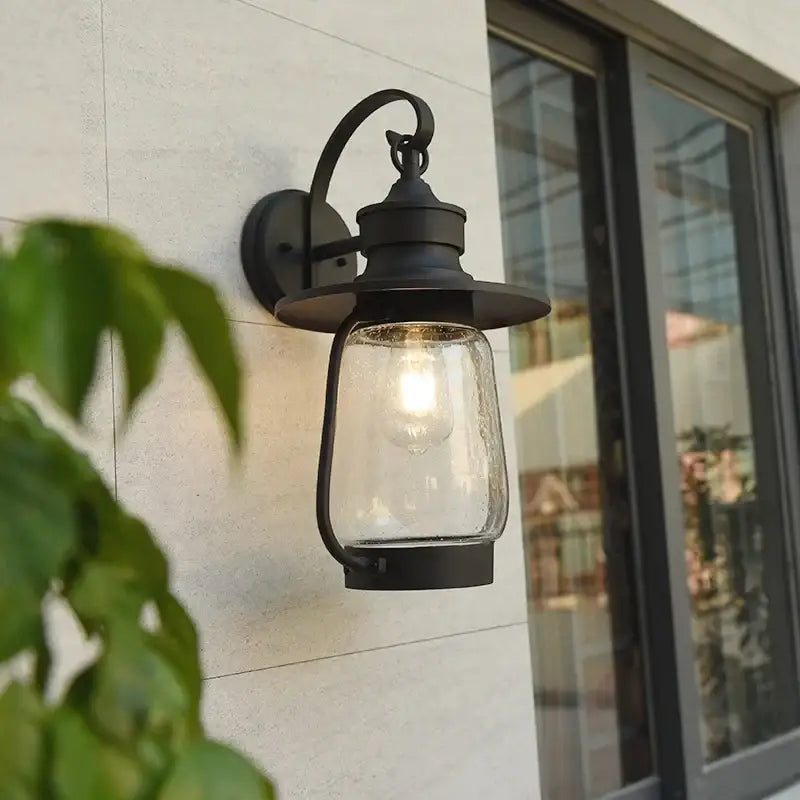 A black metal wall light with bubble glass, securely mounted onto a pale-colored wall surface.