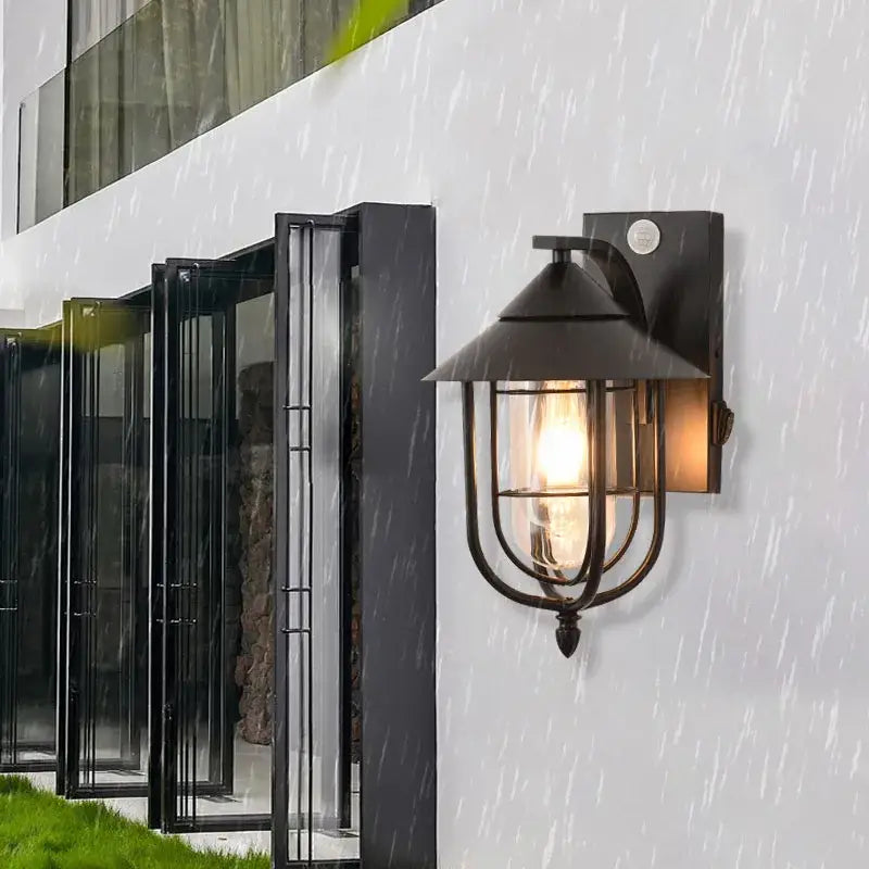 A metal outdoor wall sconce with lantern design, IP65-rated, glowing warmly in rain.