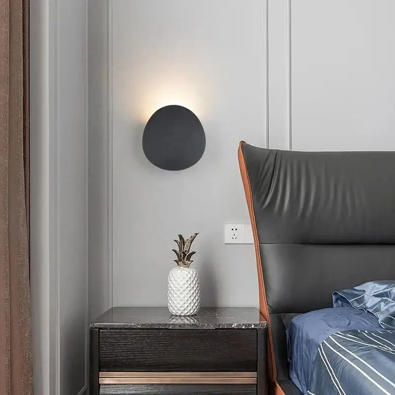 A round outdoor aluminum LED wall light mounted on a modern bedroom wall, illuminated.