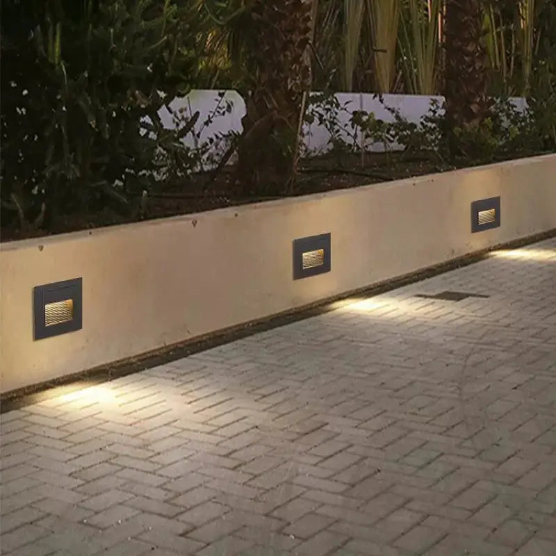 Aluminum outdoor wall spotlight designed for square or round stairs, mounted in a low garden wall.