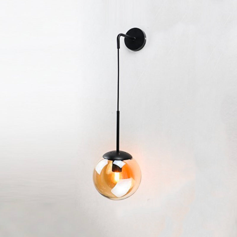 Black and gold metal wall sconce with a hanging glass sphere, casting warm light.