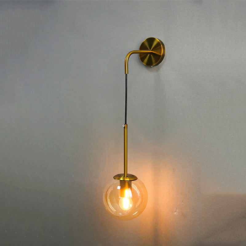 Black gold metal wall sconce with brass base, curved arm, and a hanging glass globe shade.