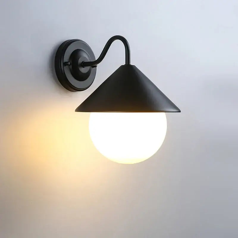 Black outdoor wall light with conical shade and white globe glass, emits warm glow.