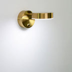 Circular brass LED wall light with flat arm and adjustable head emits soft focused glow.