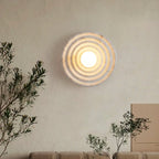 Circular glass wall light emitting concentric rings on a textured white wall, modern and elegant.
