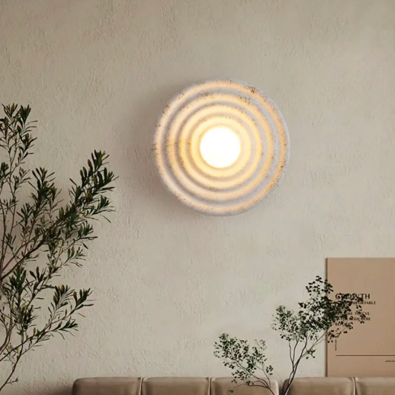 Circular glass wall light emitting concentric rings on a textured white wall, modern and elegant.