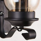 Close-up of a vintage industrial wall light with curved black metal base and glass globe shade.