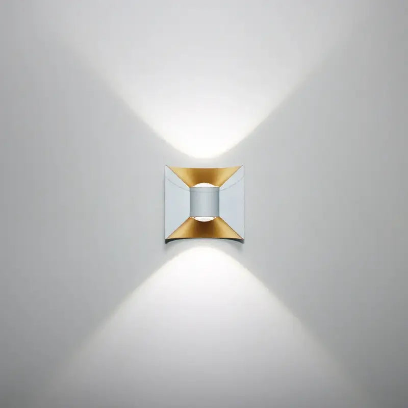 Curved aluminum LED wall light with gold and silver accents, casting hourglass-shaped beams.