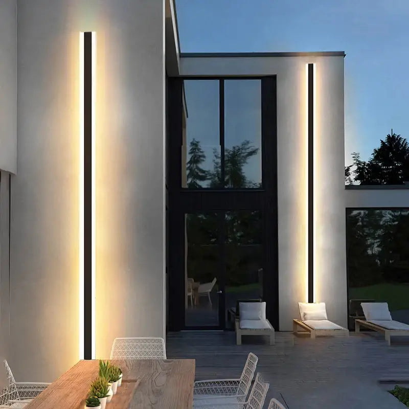 Extra Large black aluminum LED outdoor wall light, waterproof, mounted on white building at dusk.