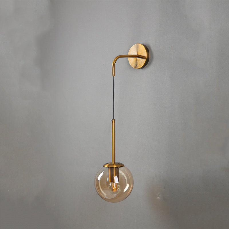 Gold and black wall sconce with a downward clear glass globe shade, modern metal design.