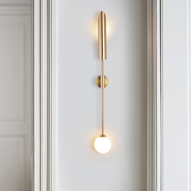 Modern golden wall light with cylindrical top and glowing spherical bulb in sleek vertical design.