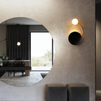 A Brushed Steel Circular Glass Wall Light glows softly against a minimalist, modern wall.