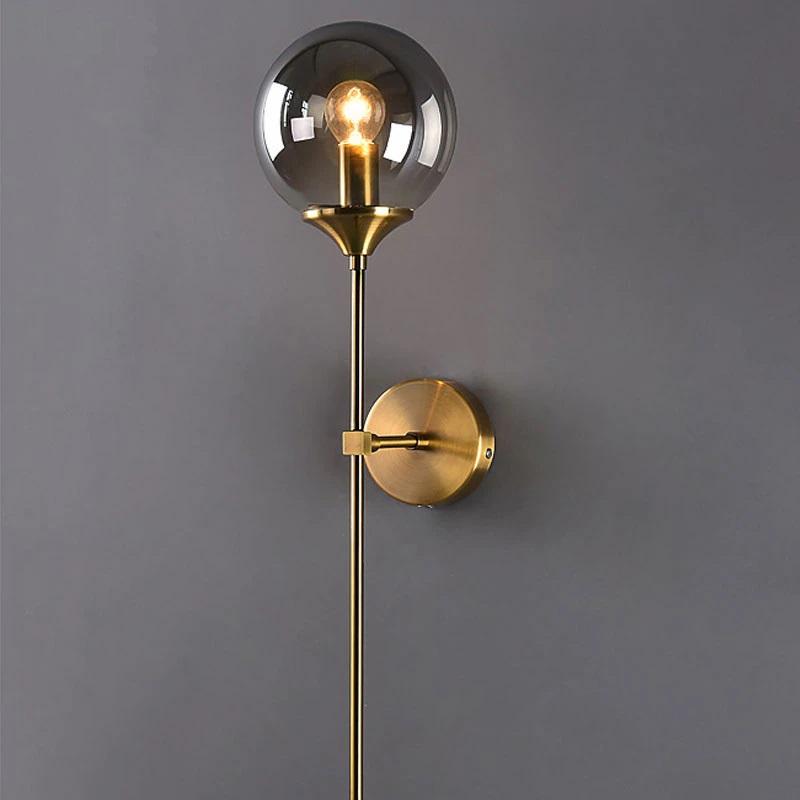 Elegant brushed steel wall light with clear smoky globe shade and glowing bulb, round base.