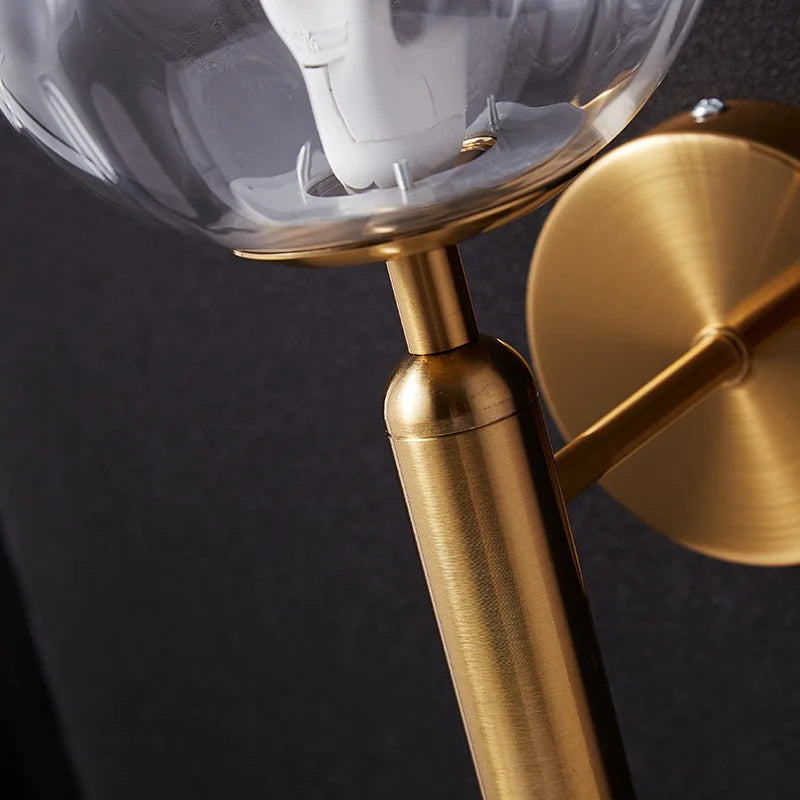 Helena glass wall light with brushed gold arm and clear globe, dark background.