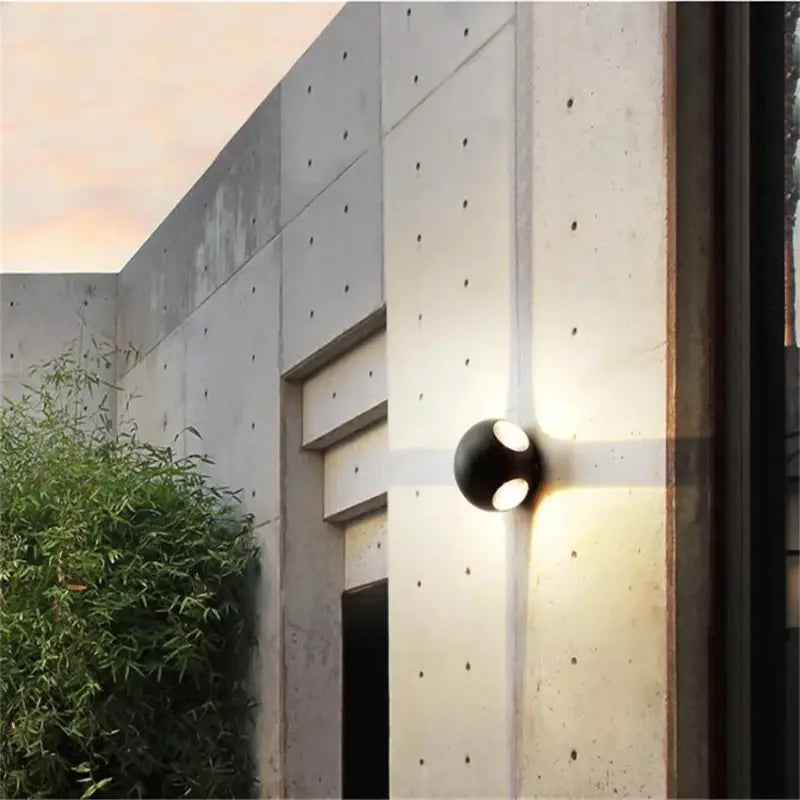 LED outdoor wall light with aluminum and glass, casting an X-shaped glow on concrete.