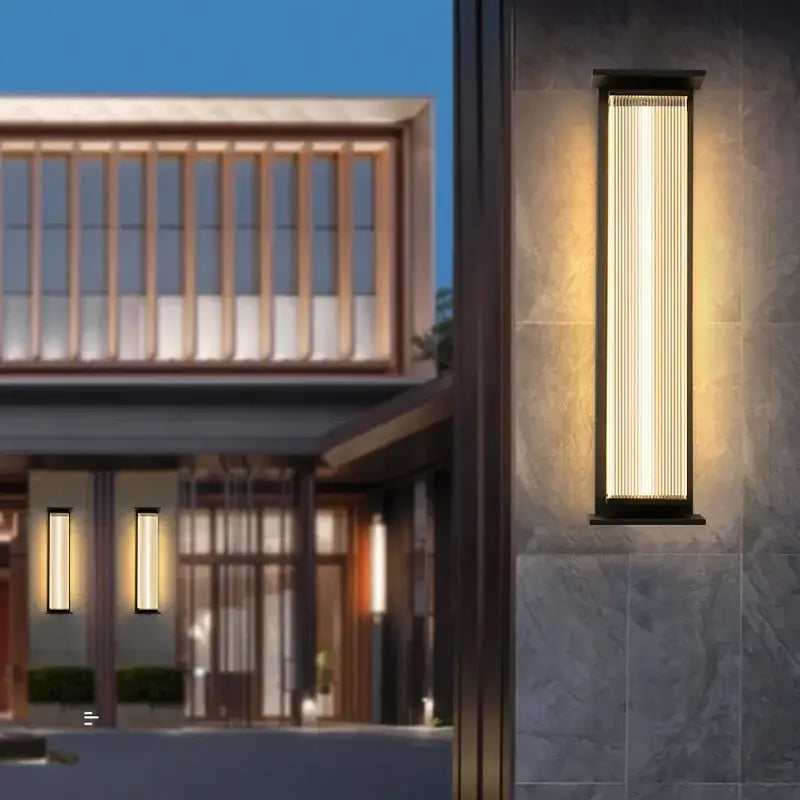 Large black glass outdoor wall light with vertical lines emits warm glow at dusk.