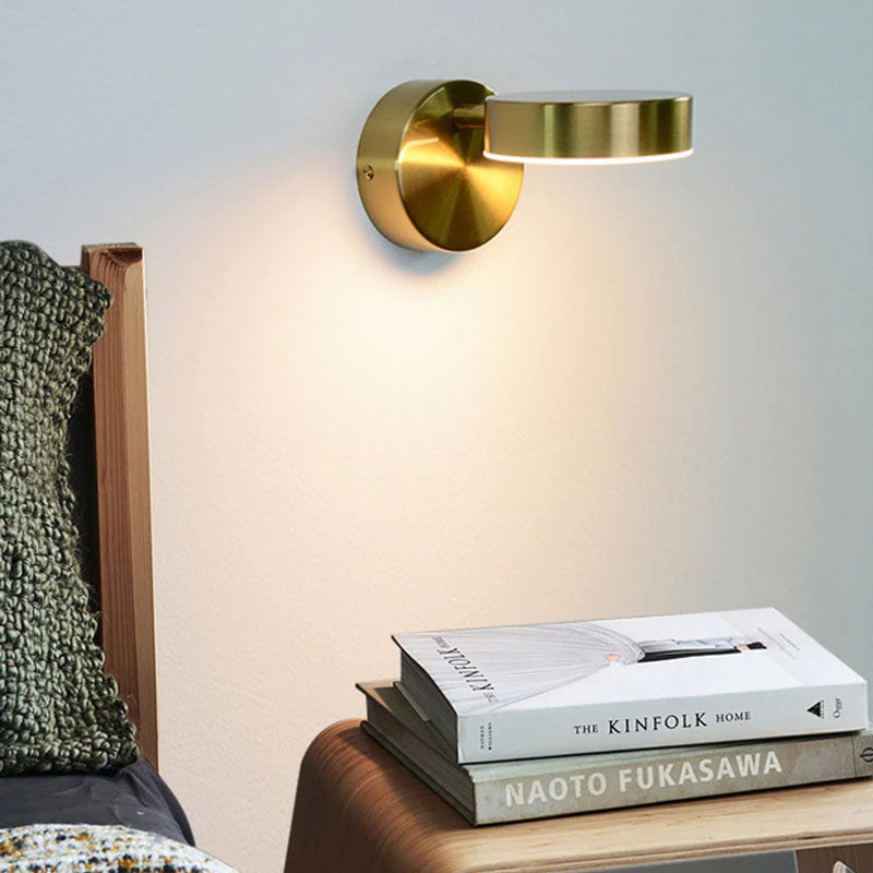 Minimalist round LED wall light with adjustable head, emitting a soft glow on the wall.