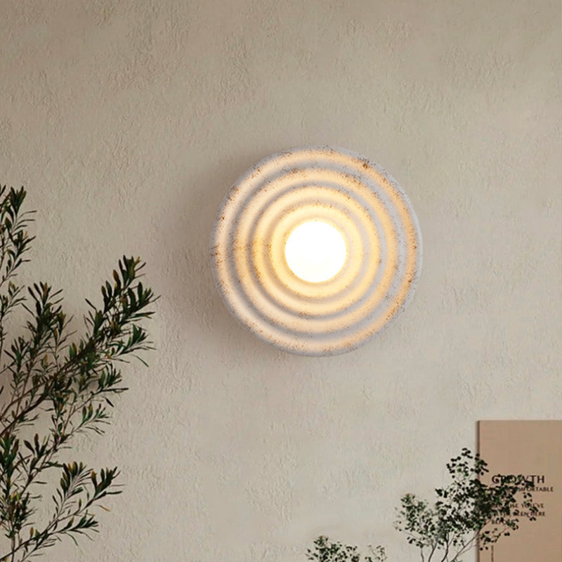 Modern circular glass wall light with concentric ridges, emitting a warm glow on beige walls.