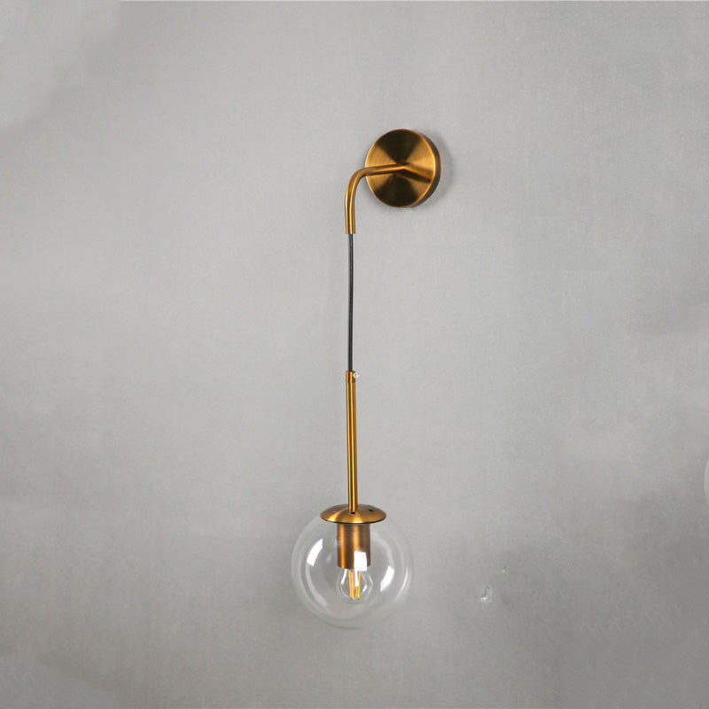 Modern wall sconce with gold frame, vertical black stem, and clear glass globe shade.