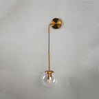 Modern wall sconce with gold frame, vertical black stem, and clear glass globe shade.