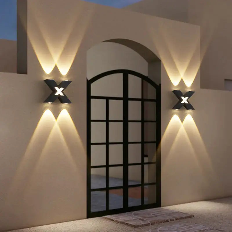 Outdoor X-shaped LED wall light casts crisscrossed beams, mounted on beige stucco wall.