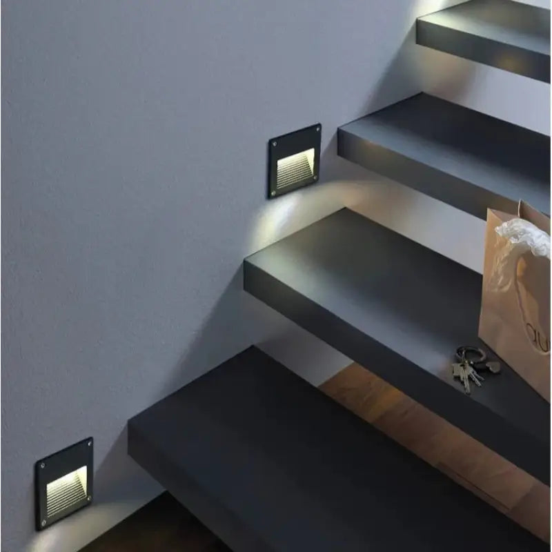 Outdoor aluminum wall spotlights are mounted, illuminating each dark gray step against a light gray wall.