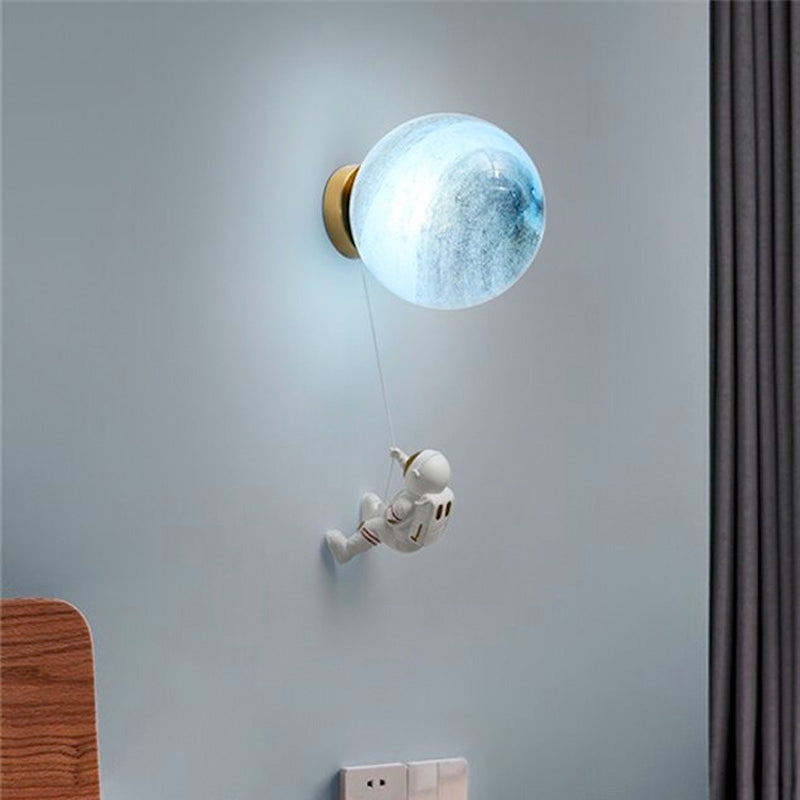 Planet Design Glass Wall Light with astronaut figurine hanging by cable, on light blue wall.