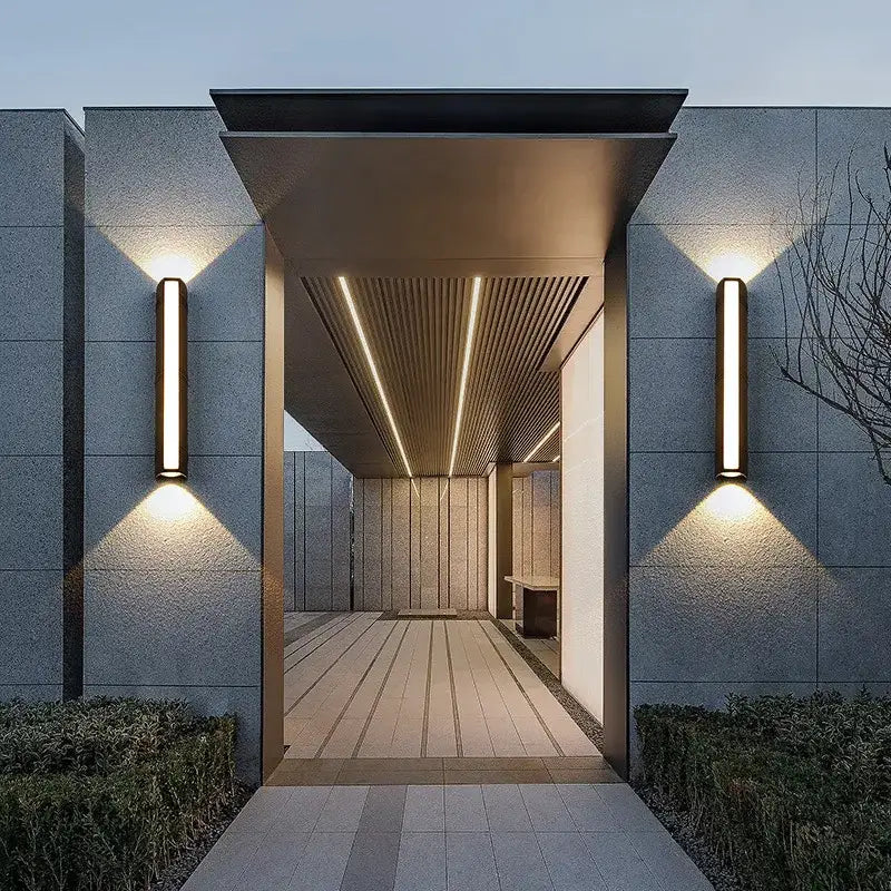 Rectangular aluminum outdoor LED wall light mounted beside a modern flat-roofed building entrance.