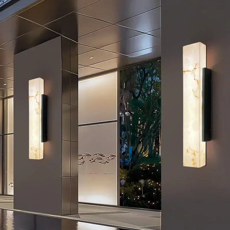 Rectangular marble-effect LED wall light mounted on facade, shade reflecting softly on wet surface.