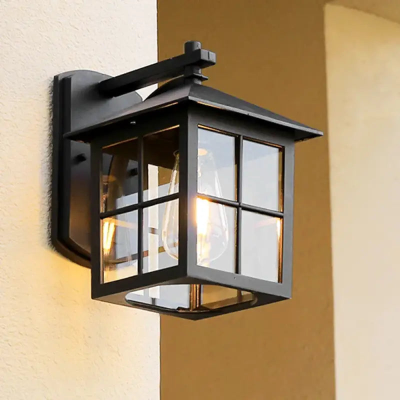 Retro metal and glass lantern wall light with clear panels, emits warm illumination.