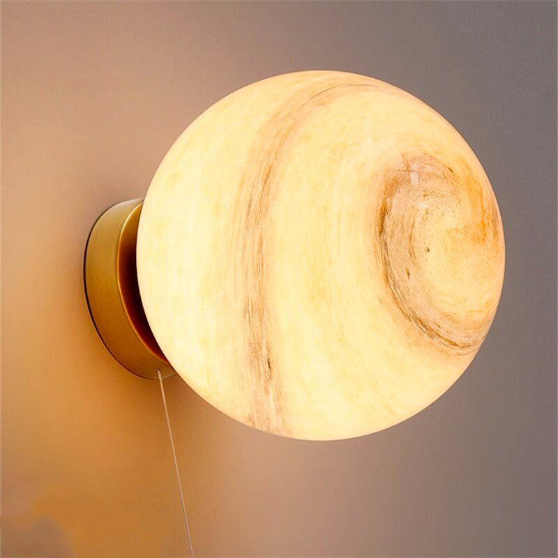 Round, moon-like marbled glass wall light with metallic base emitting a warm, cozy glow.