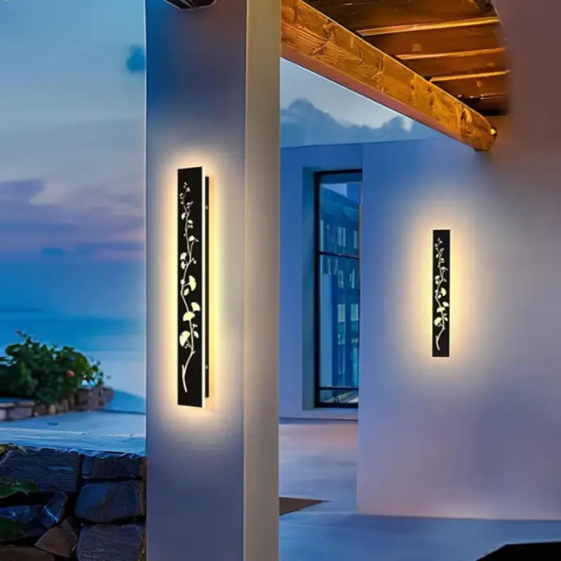 Sleek vertical aluminum wall sconce with engraved, illuminated floral design at dusk.