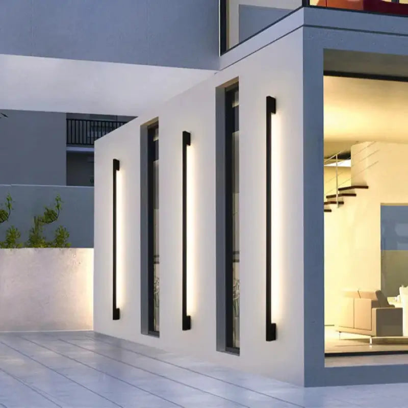 Slim Outdoor LED Wall Light in Aluminum, emitting sleek light beside tall, narrow windows.