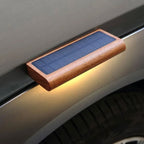 Slim rectangular outdoor solar LED wall light with a wooden frame, casting a warm yellow glow.