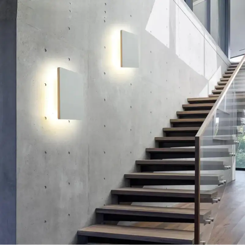 Square Aluminum Outdoor Patio Wall Light emits a soft glow against a concrete wall.