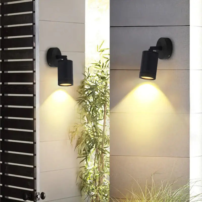 Stainless steel outdoor wall light with tempered glass, mounted and casting a warm downward glow.