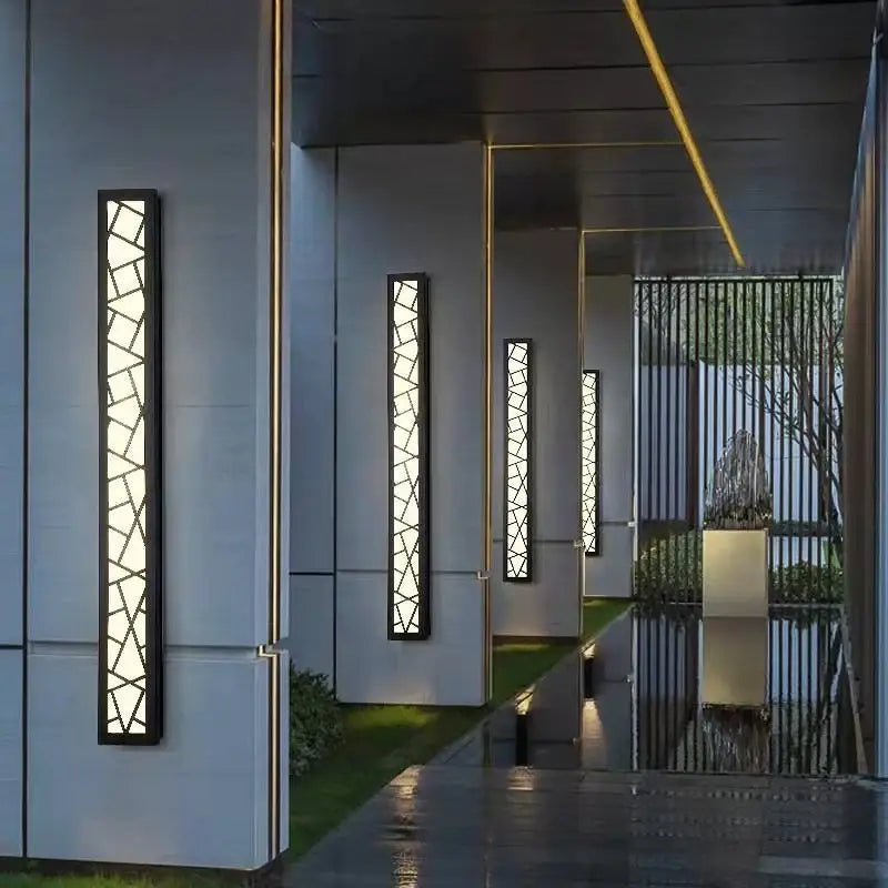 Tall, narrow aluminum wall sconce with geometric patterns casting reflections on glossy floor.